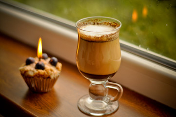Сoffee latte and a lit candle at rainy window