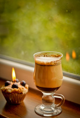 Сoffee latte and a lit candle at rainy window