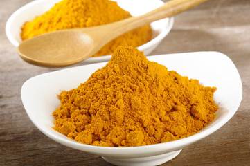 turmeric powder in white dish on wooden background