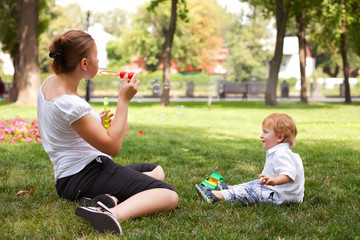 happy child and woman outdoor playing with soap bubble on meadow