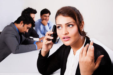 Indian businesswoman using phone with colleagues in ackground