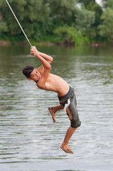 Teenage boy jumping into the river from the swinging rope