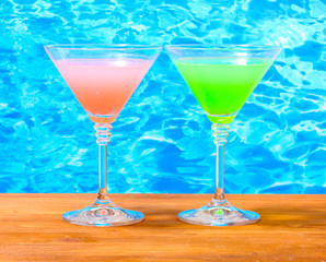 Glasses of cocktails on wooden table on blue sea background