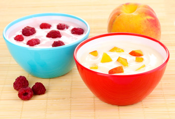 Yogurt with peaches and raspberries in bowls on bamboo mat