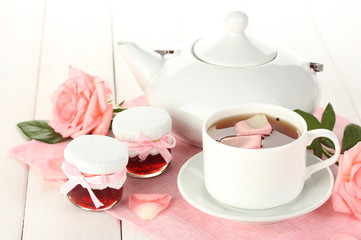 teapot and cup of tea with roses and jam on white wooden table
