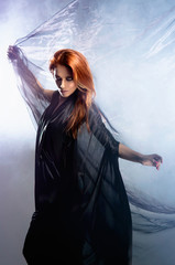 A young redhead woman in a beautiful dress covered with silk