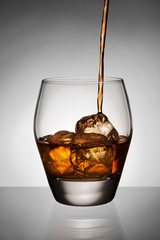 Whisky pouring on ice in glass.