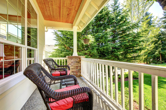 Front porch with brown chairs and red cushions.