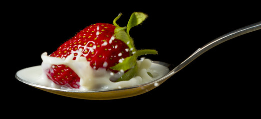 red, ripe strawberry falling in spoon with milk