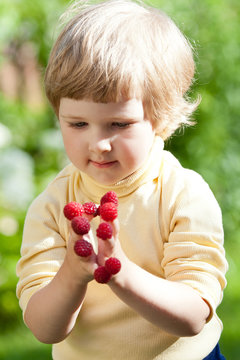 Cute little girl with raspberries on her fingers