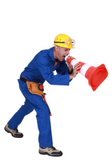 Construction worker shouting into a traffic cone