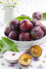 Naklejka na ściany i meble Fresh wet plums with leaves in the bowl on the vintage board