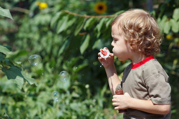 Young cute boy blowing a bubbles outdoors on a sunny day