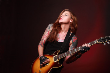Obraz premium Attractive punk girl with tattoos playing electric guitar