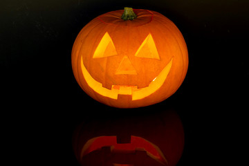 Halloween pumpkin with scary face with reflection on black glass