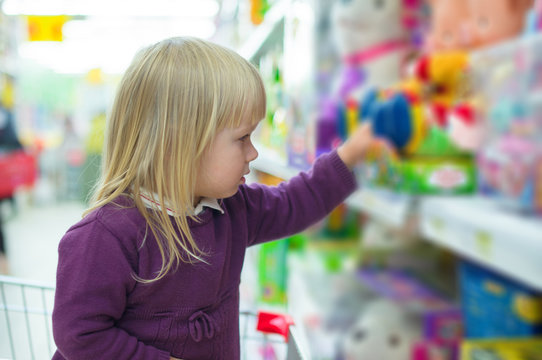 Adorable baby with toys on shelves in mall