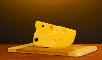 Cheese on cutting board on wooden table on brown background