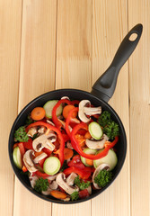 frying pan with vegetables on wooden background