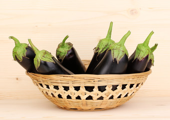 Fresh eggplants in basket on wooden background