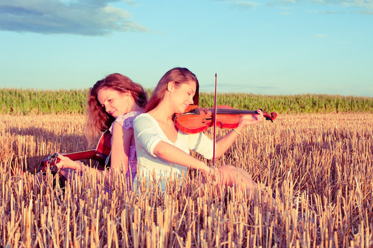 Two young women playing guitar and violin outdoors. Split toning
