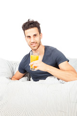 Fototapeta premium Smiling man is drinking orange juice in the bed