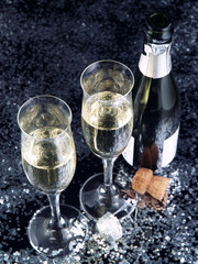 Two champagne flutes and a bottle on a black glossy background.
