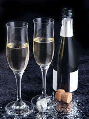 Two champagne flutes and a bottle on a black glossy background.