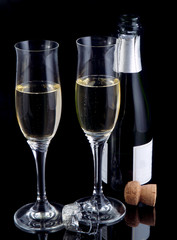 Two champagne flutes and a bottle on a black glossy background.