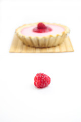 Single raspberry with raspberry tart in the background