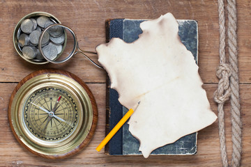 Compass, paper, book, pencil, magnifying glass, coins on wood