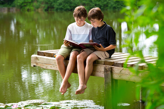Zwei jungendliche Freunde lesen ein Buch am Teich