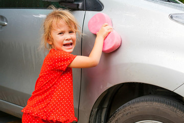 a little girl washing the car with a sponge 