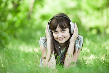 Young fashion girl with headphones at green spring grass.