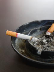 Closeup burning cigarette in ashtray and smoke on the table