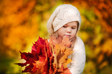 Cute little girl with autumn leaves in the park