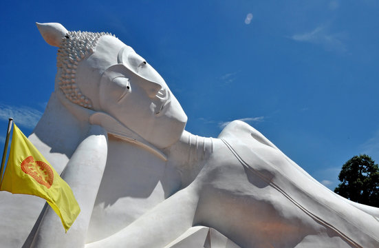 Giant reclining buddha over blue sky with buddhist flag