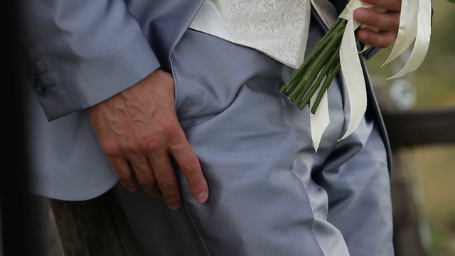Groom standing with bride's bouquet and waiting for the bride