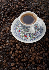 Cup of black coffee on a saucer on roasted coffee beans  