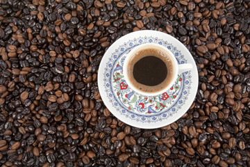 Cup of black coffee on a saucer on roasted coffee beans  