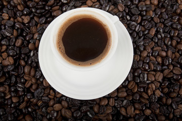 Cup of black coffee on a saucer on roasted coffee beans  