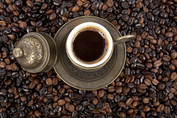 Cup of black coffee on a saucer on roasted coffee beans  