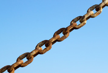 Old rusty metal chain links and a blue sky.