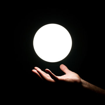 Bright light ball over human hand isolated on black background