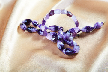 Beads and bracelet from violet glass against from a fabric