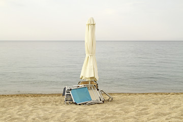 End of summer. Closed parasol and chairs on an empty beach