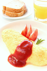 French omelet on white plate with bread and orange juice