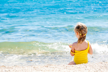 Small caucasian girl sitting on the shore of the sea