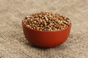 Heap coriander seeds in bowl on canvas background close-up
