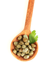 green capers in wooden spoon on white background close-up
