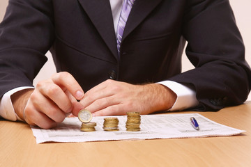 Businessman putting the coins in columns - obrazy, fototapety, plakaty